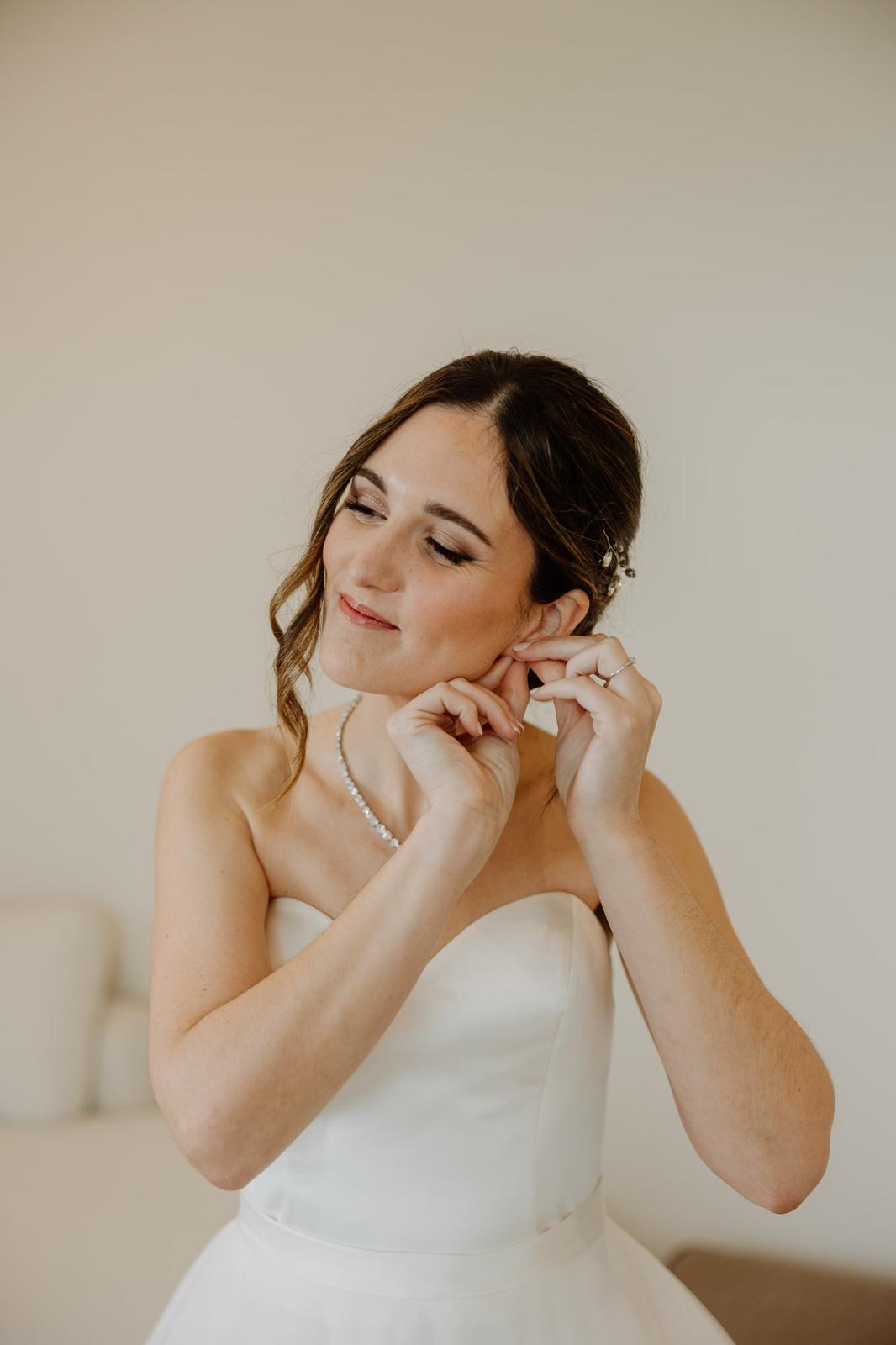 Novia colocándose los pendientes con maquillaje y peinado natural